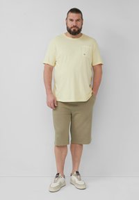 Jasnożółta bawełniana koszulka z kieszonką na piersi, w połączeniu z oliwkowymi szortami. Białe sneakersy z beżowymi akcentami dopełniają strój.