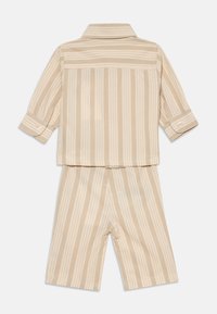 Dvojdielny detský outfit s béžovými a krémovými vertikálnymi pruhmi, dlhými rukávmi, košeľou na gombíky a zodpovedajúcimi kraťasmi po kolená.
