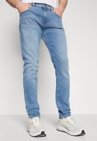 Lyseblå denimjeans med slim fit, som har fem lommer, synlig søm og en enkel finish. Bæres med hvite treningssko.