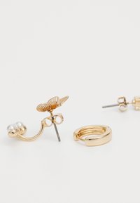 Boucles d'oreilles dorées présentant un design floral avec des détails complexes et un accent en perle, accompagnées d'une boucle d'oreille en forme de créole élégante.