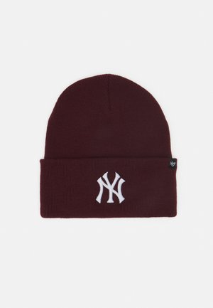 Maroon knit beanie with a rolled cuff, featuring a white embroidered logo. Soft texture, rounded top, and small brand tag on side.