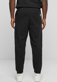 Svarte joggebukser laget av mykt stoff, med elastisk midjebånd, avsmalnede ankler og en baklomme med logodetalj.