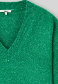 Pull vert à col en V en tricot doux, avec une finition texturée et un col en rib. Étiquette de taille visible, indiquant la taille S.