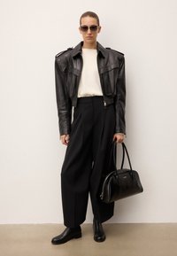 Čierna kožená skrátená bunda, krémový sveter, čierne nohavice s vysokým pásom, čierne členkové topánky, veľká čierna kabelka, minimalistický dizajn.