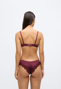 Burgundi csipkés szegéllyel ellátott melltartó- és alsóneműkészlet, állítható pántokkal és puha, sima tapintású anyagból, aprólékos csipke díszítéssel.