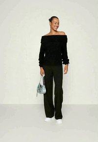 Μαύρος ριχτός πλεκτός κλινάτος πουλόβερ, χυτές μαύρες παντελόνες, λευκά αθλητικά παπούτσια και μια μικρή ιριδίζουσα τσάντα. Απαλή υφή, κα casual στυλ.