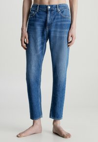 Jeans de mezclilla azul claro con un diseño de pierna recta, cinco bolsillos y cierre de botón. El dobladillo está recortado y deshilachado.