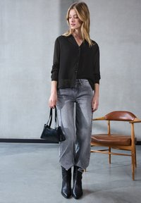 Camisa negra de botones con tela transparente y mangas largas; jeans grises de talle suelto; botas negras de tacón; bolso negro pequeño.