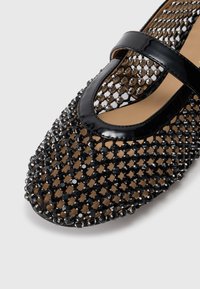 Chaussure noire de style Mary Jane avec une lanière en cuir verni et un dessus texturé avec perles, présentant un motif en maille et un intérieur lisse.