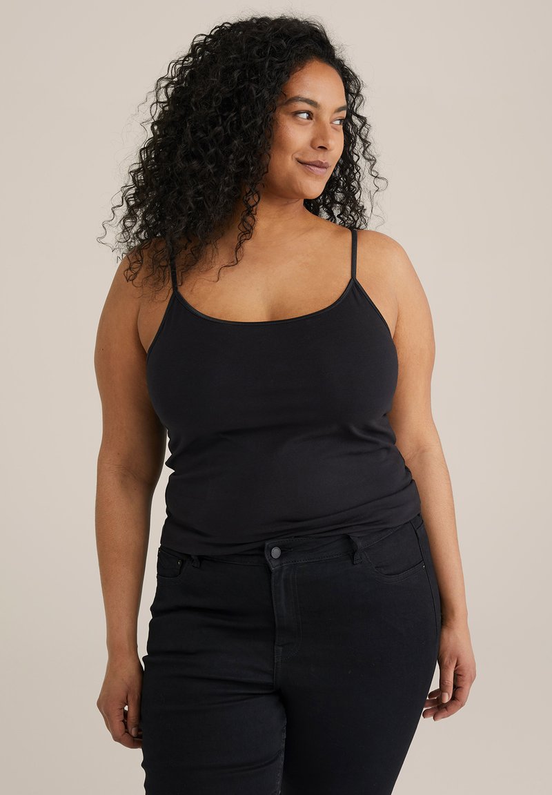 Schwarzes tailliertes Tanktop mit dünnen Trägern, kombiniert mit dunklen Jeans. Der Stoff wirkt glatt und hat einen leichten Stretch. Minimales Design und keine sichtbaren Muster.