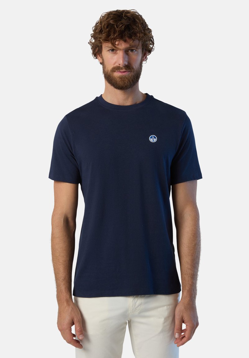 T-shirt in cotone blu navy con maniche corte e scollatura a girocollo, con un piccolo logo rotondo sul lato sinistro del petto. Texture liscia.