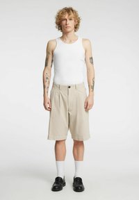 Jasnobeżowe plisowane szorty z dwoma przednimi kieszeniami, zestawione z białym topem na ramiączkach. Dopełnieniem stroju są czarne buty wsuwane i białe skarpetki do kostek.