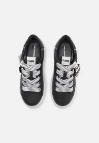 Baskets en cuir noir avec des accents blancs, présentant un laçage en mesh texturé et une languette de marque. La semelle est blanche et épaisse.