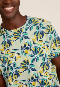 Korte mouwen t-shirt in lichtgroen, voorzien van een bloemendessin met marineblauwe, gele en teal bloemen. Ribbeltextuur bij de halslijn.