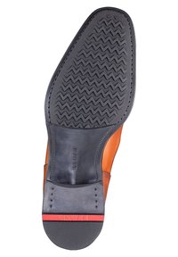 Ruskea nahkakenkä mustalla kumipohjalla, jossa on sahalaitakuviomalli, tyylikäs muotoilu ja punainen yksityiskohta kantapään lähellä.