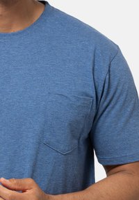 Lyhythihainen sininen t-paita, joka on valmistettu rakenteellisesta, kevyestä kankaasta ja jossa on yksi rintatasku sekä pyöreä kaulus.