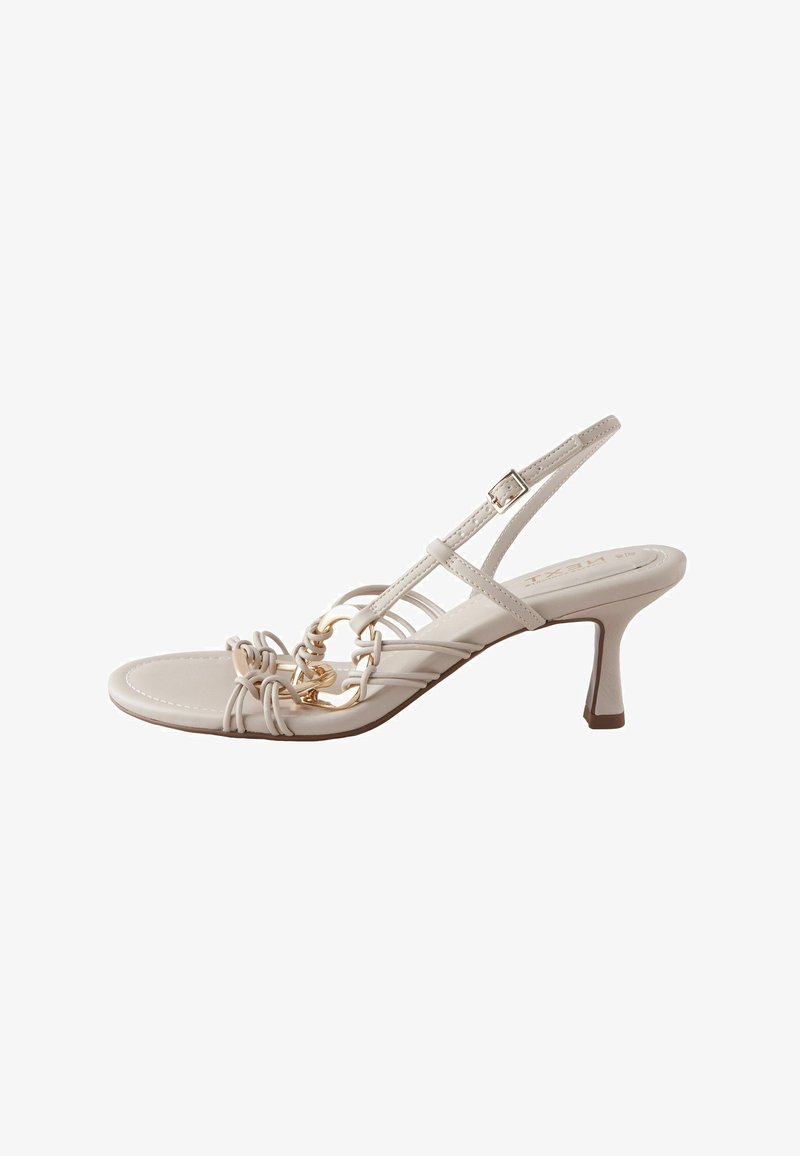 Beige slingback sandal with a low heel, featuring delicate intertwined straps and a gold chain accent. Smooth leather texture, minimalistic design.