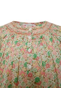 Vestito floreale con bottoni realizzato in cotone leggero. Presenta fiori rosa, verdi e gialli su uno sfondo bianco, con dettagli a pintuck e smocking.