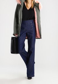 Dunkelblaue, hoch geschnittene Hosen haben einen geraden Schnitt, mit einer Stoffstruktur, die Denim ähnelt, und drei dekorativen Knöpfen an der Seite.