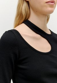 Schwarz geripptes Langarmoberteil mit einem einzigartigen Ausschnitt-Design an der Schulter. Glatte Textur mit einer taillierten Silhouette und rundem Ausschnitt.