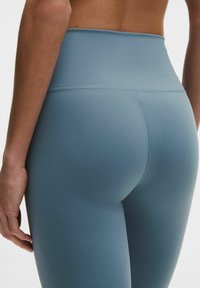 Leggings de talle alto en un tejido azul claro, con una textura suave y diseño elegante con una costura visible a lo largo de la parte trasera.