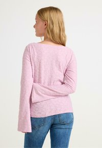 Lichtroze langlopende top met een textuur van bloemenpatroon, brede mouwen en een bootnek, gecombineerd met blauwe denim jeans.