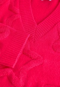 Světlý růžový svetr s výstřihem do V, žebrovaným límcem a texturovaným zigzag vzorem, vyrobený z měkkého a huňatého materiálu.