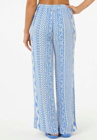 Blaue gemusterte weite Hosen mit geometrischen Designs. Der Stoff zeigt eine Mischung aus karierten und Sternmotiven. Elastischer Bund.