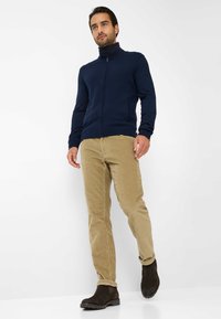 Maglione navy con zip, pantaloni in corduroy beige, stivaletti alla caviglia marroni scuri. Il maglione presenta un colletto alto. Texture liscia, design aderente.