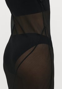 Fekete áttetsző anyagú ruhadarab, szilárd fekete részletekkel, texturált felülettel és ellentétes átlátszatlan részekkel az alján.