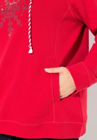 Felpa rossa con un design a fiocco di neve testurizzato, polsini a coste e tasca frontale. Presenta un cappuccio con coulisse dal design intrecciato a contrasto.
