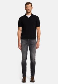 Schwarzes Poloshirt mit kurzen Ärmeln und Reißverschlusskragen, kombiniert mit schmal geschnittenen grauen Jeans und braunen Lederschuhen. Glattes Material und modernes Design.