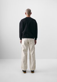 Sweatshirt noir à coupe décontractée, associé à un pantalon cargo crème, avec des poches latérales et des accents zippés, vu de dos.