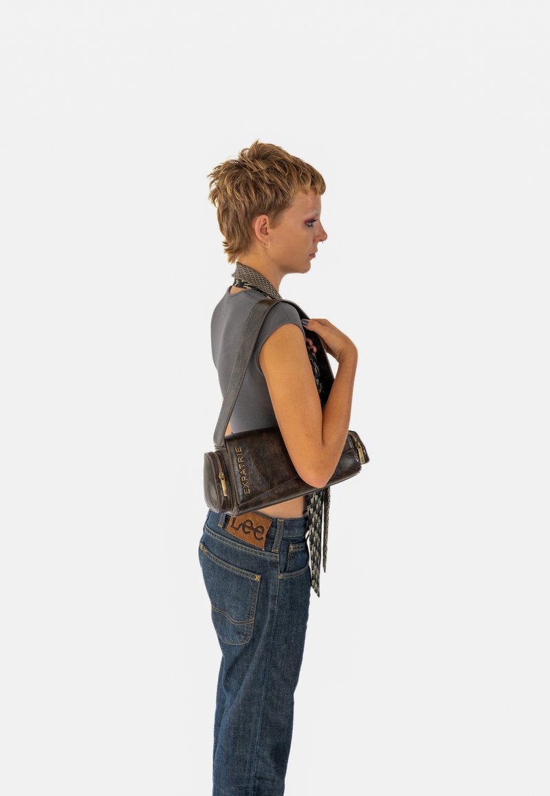 Sac à main en cuir marron avec une forme structurée, une sangle réglable et une fermeture éclair. Logo de marque notable embossé à l'avant.
