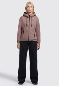 Helle rosa Kapuzenjacke mit elastischen Bündchen und Reißverschlusstaschen, kombiniert mit schwarzen Cargo-Hosen mit mehreren Taschen.