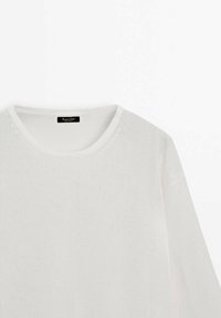 Pull en maille blanche avec un col rond et une coupe décontractée. Texture douce, manches longues et détails de couture subtils le long du col.