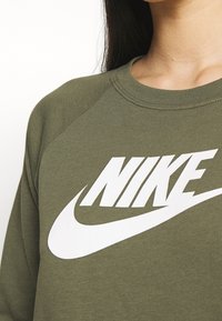 Olivgrön sweatshirt med rund halsringning och långa raglanärmar. Har en stor vit Nike-logotyp som är tydligt synlig på framsidan.