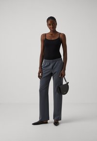 Black tank top, gray wide-leg trousers with elastic waist, black flat shoes, textured black handbag with a chain. Plain background.