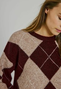 Bordo unbeige argyle raksta adīta džemperis ar apaļu apkaklīti un mīkstu tekstūru, kurā iezīmējas diagonāla šuvju līnija uz dimanta formām.