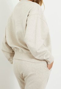 Sudadera gris claro hecha de una tela suave y texturizada, con un escote redondo, hombros caídos y puños acanalados, combinada con pantalones a juego.