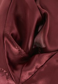 Gros plan sur un tissu satin bordeaux lisse avec des coutures visibles et un texte brodé subtil le long du bord.