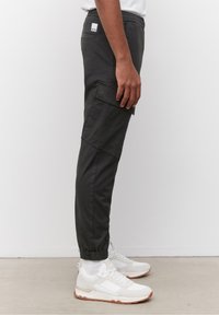 Černé cargo kalhoty s elastickými manžetami, bočním nákladním kapsou a slim fit střihem, kombinované s bílými teniskami s gumenou podrážkou a síťovými detaily.