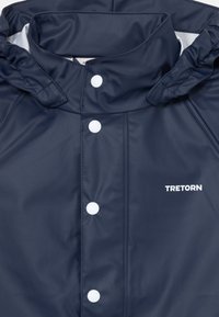 Marinevannavot med høyt krage, hvite trykknapper og "TRETORN" logoen trykt i hvitt på forsiden. Glatt tekstur.