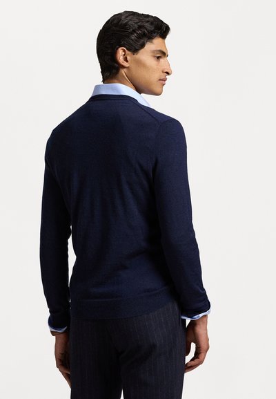 Suéter de punto ligero azul marino con mangas largas, dobladillo acanalado y textura sutil, llevado sobre una camisa de vestir azul claro.
