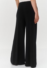 Czarne spodnie szerokie z gładką fakturą i elastycznym pasem, o swobodnym kroju, sięgające do kostki.