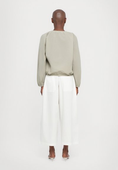 Blusa grigia chiara, a maniche lunghe con polsini elasticizzati, aderente all'orlo, abbinata a pantaloni bianchi larghi con tasche posteriori.