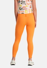 Leggings arancioni realizzati in materiale elastico, con una texture liscia, forma aderente e dettaglio con zip alla caviglia. Accento elegante in vita.