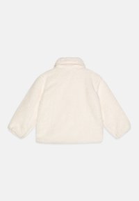 Giacca morbida e fluffy di colore crema realizzata in materiale pile, con collo e maniche ampie, caratterizzata da un design semplice e minimale.