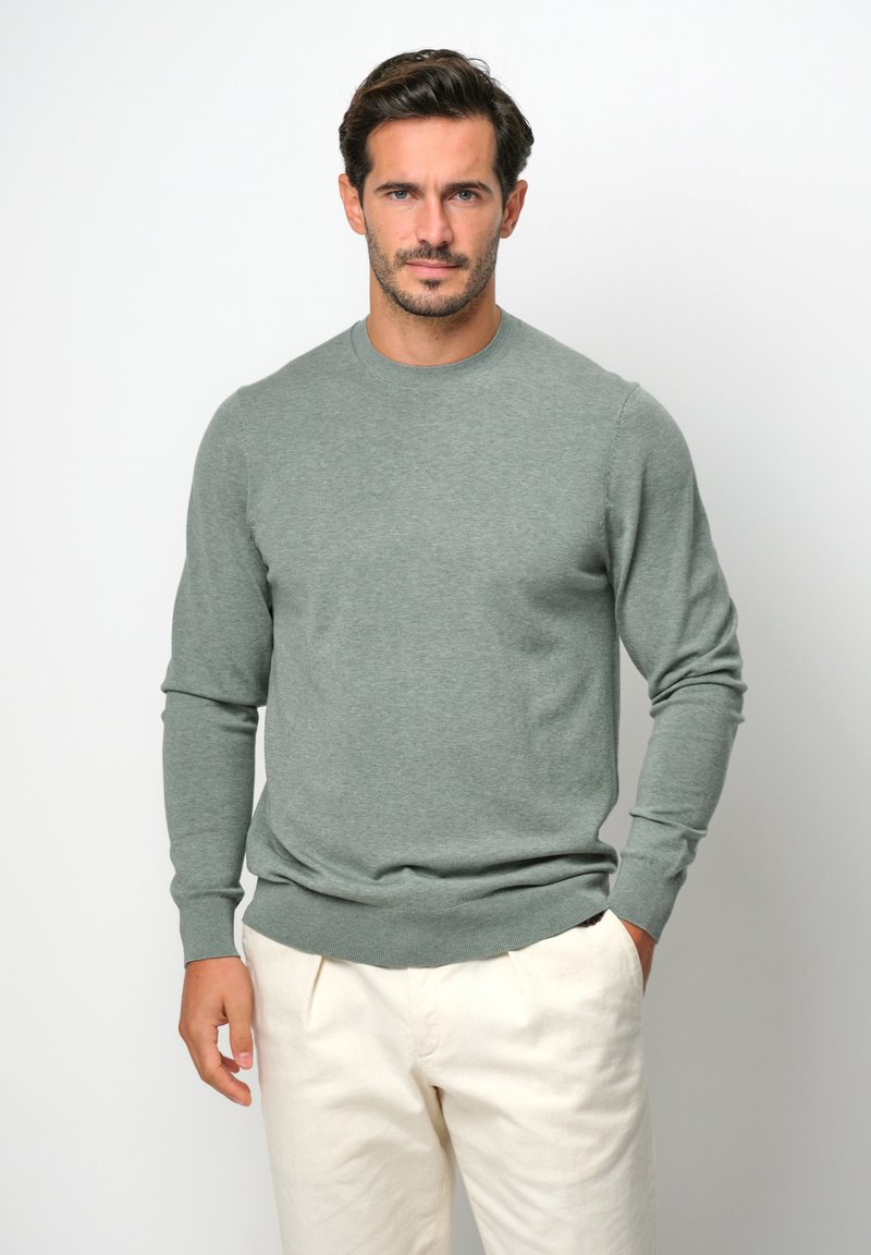 Maglione lavorato a maglia verde chiaro con scollo rotondo, polsi a coste e orlo a coste. Abbinato a pantaloni beige chiaro, caratterizzati da una vestibilità comoda e tasche laterali.