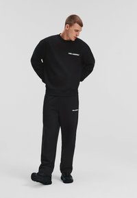 Conjunto de sudadera y pantalones negros con el logo bordado "Karl Lagerfeld" en blanco. La tela parece suave; ajuste holgado con puños acanalados.